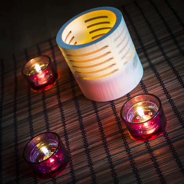 Tea candles in wood and glass standing on reed mat — Stock Photo, Image