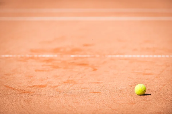 Yellow tennis ball on orange sand and white lines — Stock Photo, Image