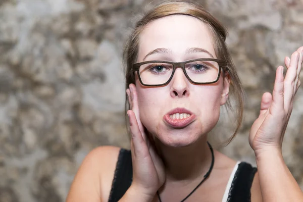 Young woman in glasses clowning around pullinga funny face jutting out her lower jaw with copyspace — Stock Photo, Image