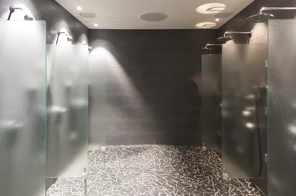 Several showers seperated with walls of glass and wall and floor with dark tiles — Stock Photo, Image