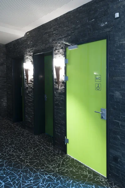 Toilettentür aus Plexiglas in einem Schwimmbad mit dunklen Fliesen und Flambeus als Licht — Stockfoto
