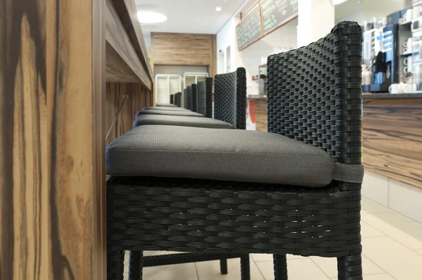 Aligned high rattan chairs with seat-contact surface in front of wooden table in self service restaurant — Stock Photo, Image