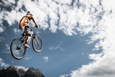genç çocuk yüksek dağlar ve gökyüzü önünde bisiklet ile atlar.
