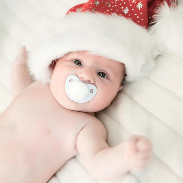 Xmas baby with santa claus cap and pacifier lying on white blanket — Stock Photo, Image