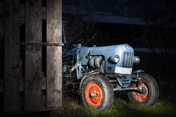 Niebieski oldtimer hodowli ciągnik stojący obok drewnianej chacie w nocy z czerwonym malowane opony — Zdjęcie stockowe