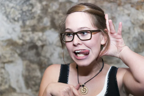 Aantrekkelijke toevallige jonge vrouw in steekt uit haar tong tegen een gevlekt achtergrond met copyspace bril — Stockfoto