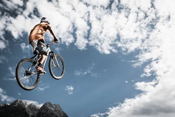 Giovane ragazzo salta in alto con la sua moto di fronte alle montagne e al cielo — Foto Stock