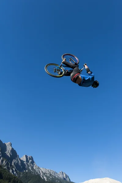 Dirt biker makes a high backflip with blue sky and mountains in the background — Stock Photo, Image