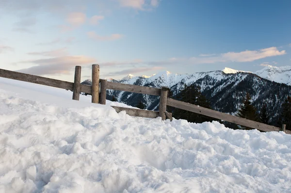 Romantiche montagne tirolesi al crepuscolo con tanta neve, recinzione in legno e cielo azzurro nuvoloso — Foto Stock