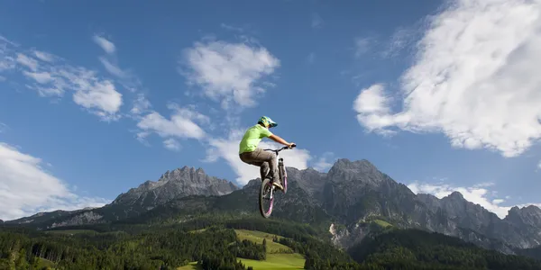 Junger Freestyler springt mit seinem BMX hoch in die Luft mit schöner Natur, Bergen und bewölktem Himmel im Rücken — Stockfoto