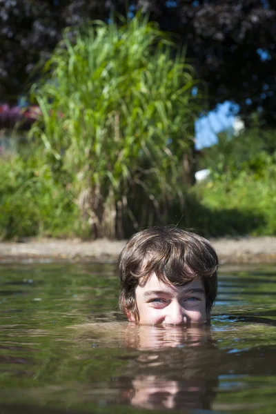 Menino é com metade de sua cabeça na água do lago zell am ver com arbusto verde na parte de trás Imagens Royalty-Free