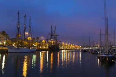 hileli bir bira bardağı ve boyunda yelkenli gemi limanda suya yansıyan renkli kentin ışıkları ile huzurlu bir sakin liman ile nightscene