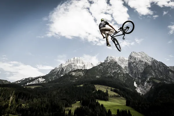 Giovane freestyler salta con la sua bmx alto in aria con bella natura, montagne e cielo nuvoloso nella parte posteriore — Foto Stock