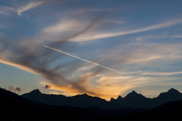 Beautiful orange sunset and contrail from a jet aifcraft over a rugged silhoutted mountain range — Stock Photo, Image