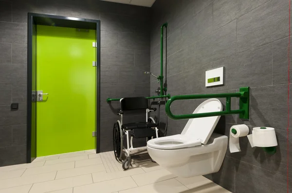 Un bagno per disabili con sbarre verdi, sedia a rotelle e porta — Foto Stock