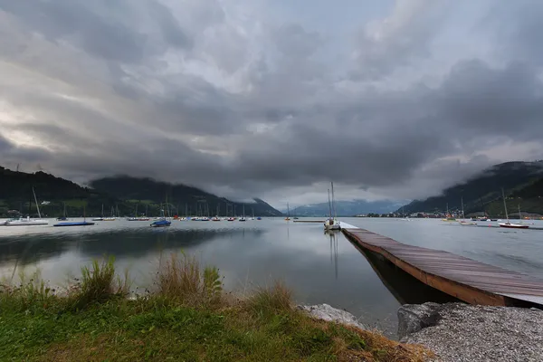 Una vista sobre un hermoso lago tranquilo y embarcadero de madera con espejo de agua tranquila bajo nubes grises amenazantes, conceptual del dicho La calma antes de la tormenta —  Fotos de Stock
