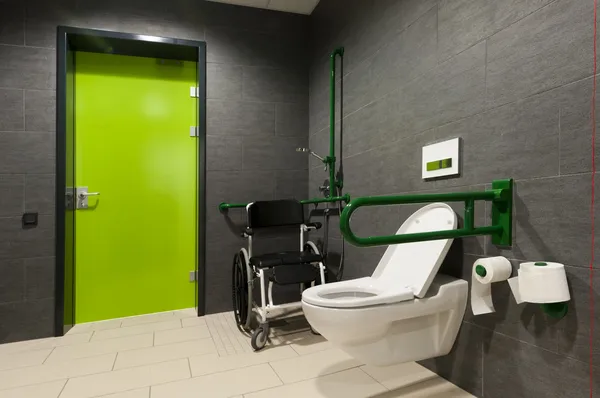 Een toilet voor gehandicapten met groene balken, rolstoel en deur Stockafbeelding
