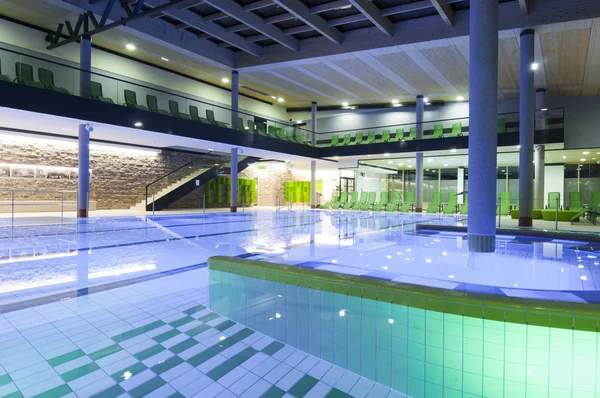 Filled indoor swimming pool with colored tiles and illumination — Stock Photo, Image