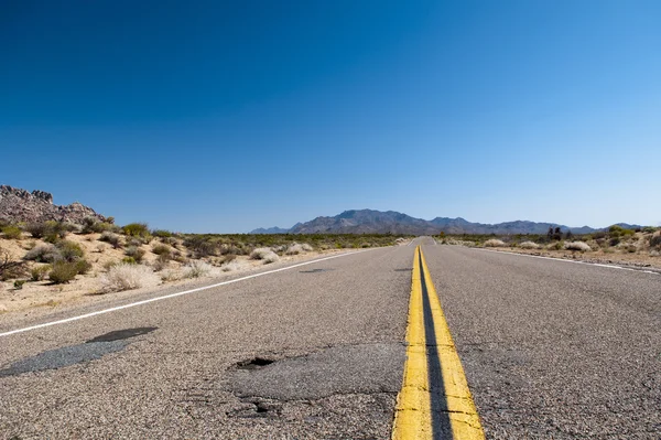 A obsolete asphaltic road with orange medial strip going threw a desert in the USA — Stock Photo, Image