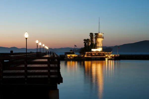 Lighted tower beacon with restaurant next to a catwalk at dawn with nice mirroring in the water — Stock Photo, Image