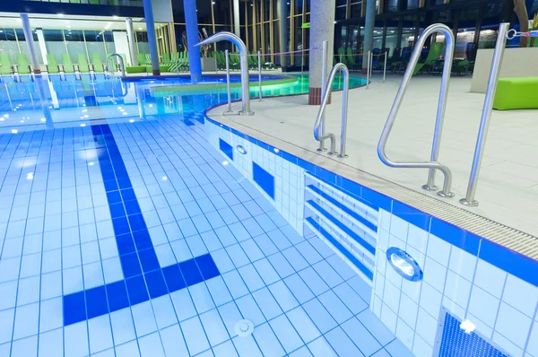 Piastrelle piscina con acqua limpida e luci con divani verdi sullo sfondo — Foto Stock