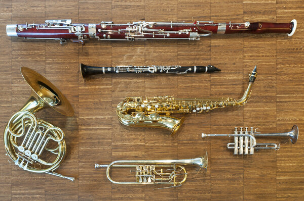 Several wind instruments laying on a wooden floor. trumpet, horn, saxophone, clarinet, flute, bassoon, curtal