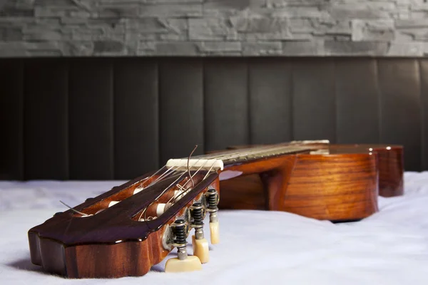 Classical guitar lying on the bed in front of a brown leather back and a stone wall — Stock Photo, Image