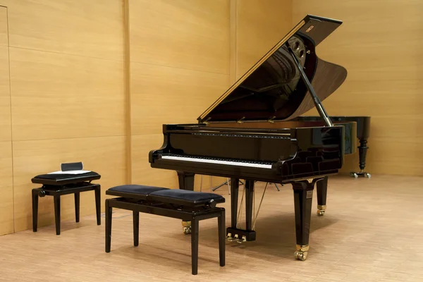Un piano negro listo para tocar con taburete delante en un escenario de madera —  Fotos de Stock