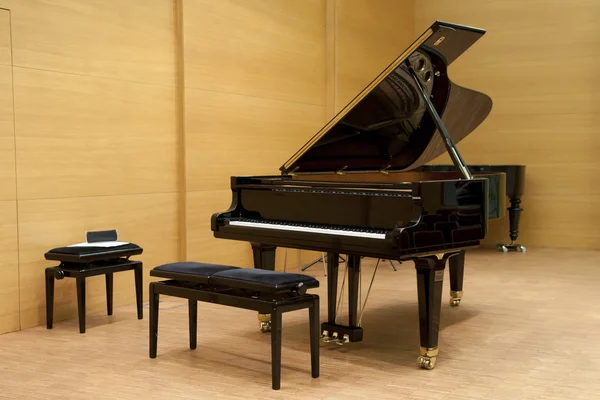 A black piano ready for playing with stool in front on a wooden stage — Stock Photo, Image