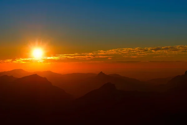 Puesta de sol entre montañas y nubes con cielo rojo — Foto de Stock