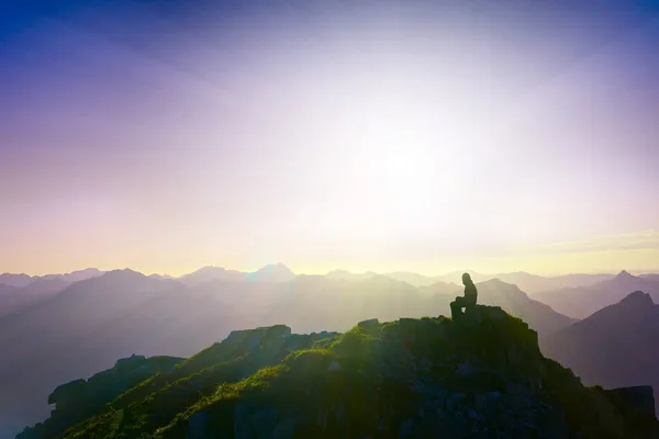 Lonely sad girl sitting on mountain summit looking over alps