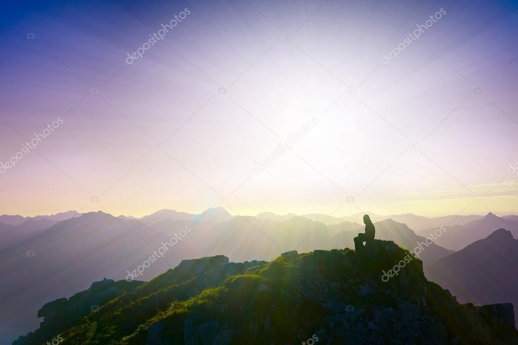 Lonely sad girl sitting on mountain summit looking over alps