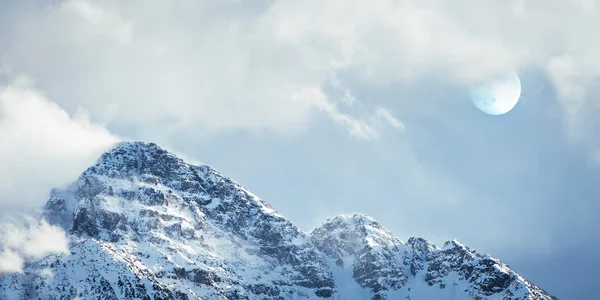 Gipfel des schneebedeckten Berges mit Nebel und Mond hinter Wolken — Stockfoto