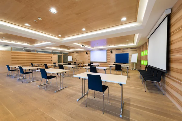Moderne houten conferentieruimte met tafels een stoelen en projectorscherm Stockafbeelding