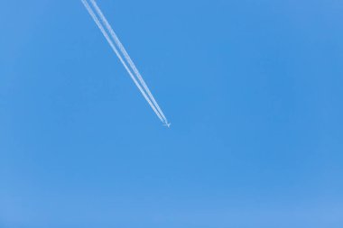 Bulutsuz mavi gökyüzünde bir uçak. Uçağın arkasında motor izleri var..