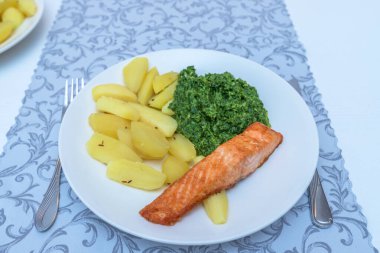 Beyaz tabakta fırında somon, patates ve yeşil ıspanak. Öğle yemeği için lezzetli yemekler..