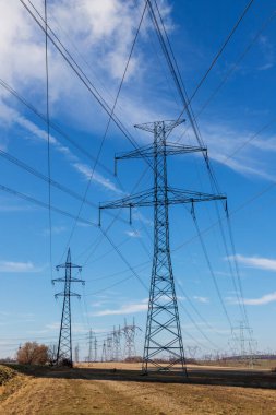 Kırsal kesimde elektrik dağıtımı için yüksek voltaj kutupları. Arka planda dramatik bulutlarla dolu mavi bir gökyüzü var..