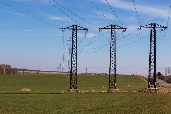High voltage poles for electricity distribution in the countryside. In the background is a blue sky with dramatic clouds.