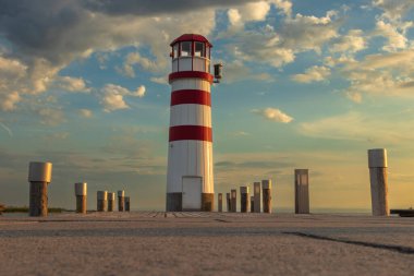 Göle giden bir iskele ve Avusturya 'nın Podersdorf kentindeki Neusiedl Gölü' nde kırmızı beyaz bir deniz feneri. Arka planda gün doğumunda dramatik bir gökyüzü var..