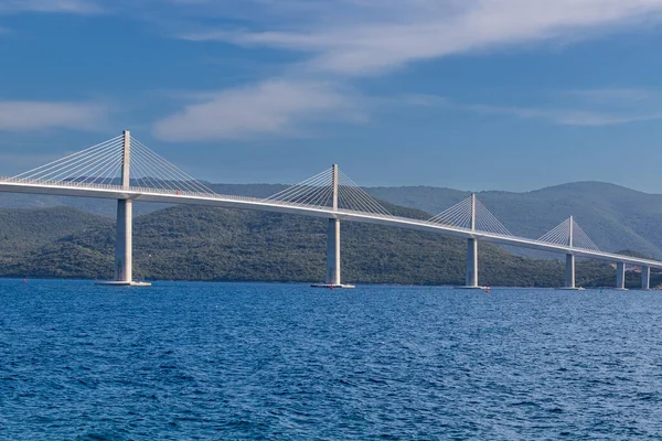 Beautiful modern bridge over the sea on Peljesac in Croatia. In the foreground houses and in the background the Peljesac mountains. Dramatic sky with clouds.