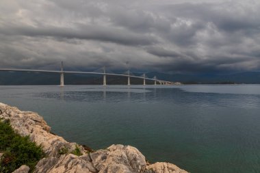 Beautiful modern bridge over the sea on Peljesac in Croatia. In the foreground houses and in the background the Peljesac mountains. Dramatic sky with clouds.