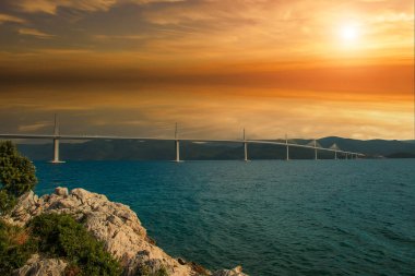Beautiful modern bridge over the sea on Peljesac in Croatia. In the foreground houses and in the background the Peljesac mountains. Dramatic sky with clouds.