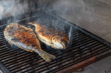 Two sea fish on the grill are being grilled on barbecue coals.