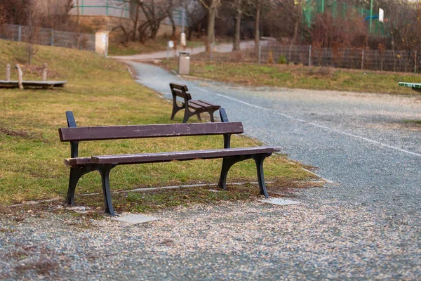 A wooden bench on a gravel path in a park. The bench is broken.