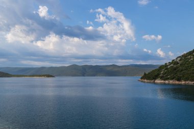 Hırvatistan 'ın Uvala-Duboka kentindeki deniz manzarası. Deniz, dağlar ve arkasında bulutlar olan mavi gökyüzü..