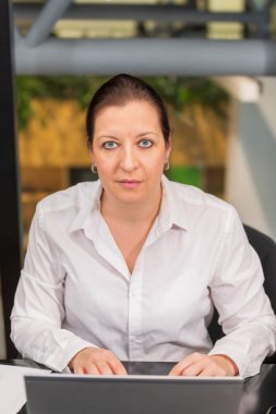 40 yaşlarında genç beyaz bir kadın bilgisayarın masasında oturuyor..