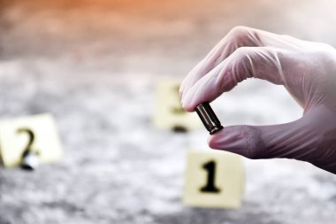 Adli memur elinde silah kovanı ya da tabanca mermisi tutuyor. Bu da olay yerinde kanıt toplarken önemli bir kanıt. Yumuşak ve seçici odak.