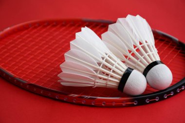 Beyaz badminton topu ve raket kırmızı zeminde, badminton kortunda, kopyalama alanı, mekik horozlarına yumuşak ve seçici odaklanma.