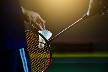 Badminton raketi ve badminton horozu erkek oyuncunun ellerindeyken, o topu ağda servis ederken, yumuşak ve seçici bir şekilde odaklanıyor. badminton spor konsepti.