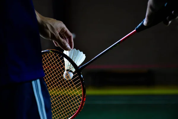 Badminton raketi ve badminton horozu erkek oyuncunun ellerindeyken, o topu ağda servis ederken, yumuşak ve seçici bir şekilde odaklanıyor. badminton spor konsepti.